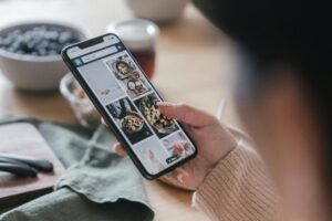 Close-up of a hand holding a smartphone browsing food recipes. Cozy kitchen setting.